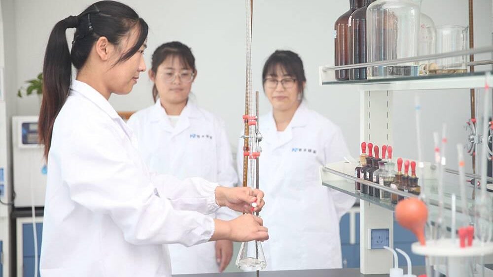 Female chemist with colleagues conducting precise experiment with burette in certified laboratory