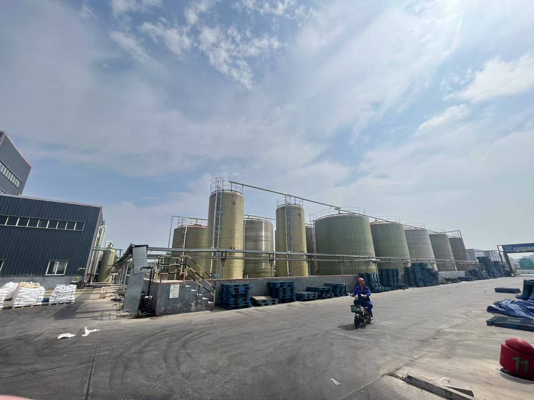 Large industrial plant with rows of storage tanks and worker on electric scooter in foreground