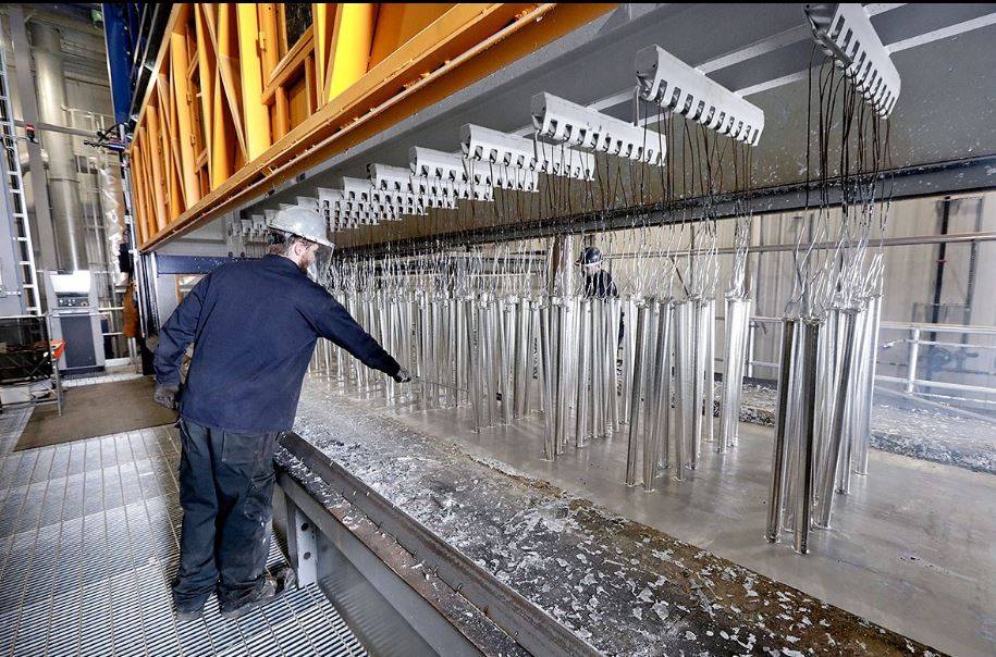 Workers overseeing automated galvanizing process with hanging metal parts in zinc bath