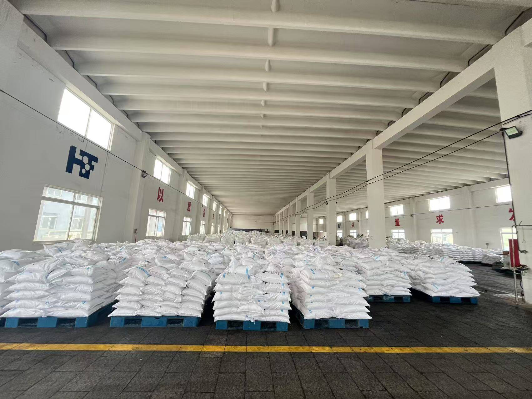 Large warehouse with neatly stacked pallets of white zinc chloride bags under high ceiling