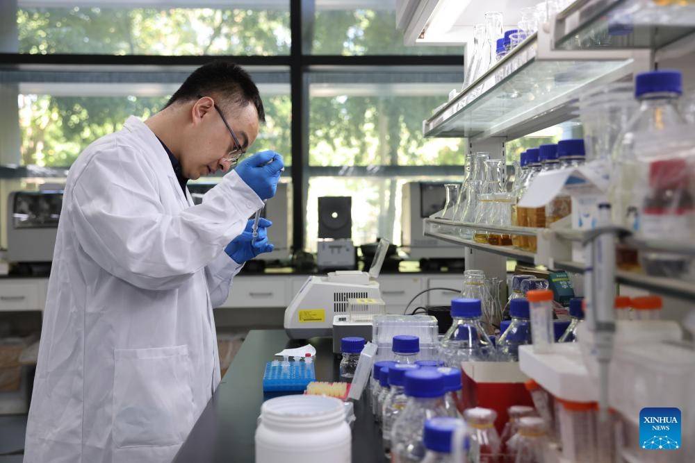 An Asian Chinese scientist in a white lab coat working with complex glassware and chemical solutions in a modern research facility.