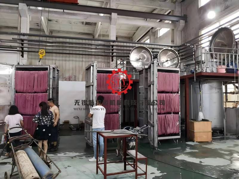 A faceless view of a large-scale industrial textile dyeing machine with pink fabric being processed in a modern factory setting.