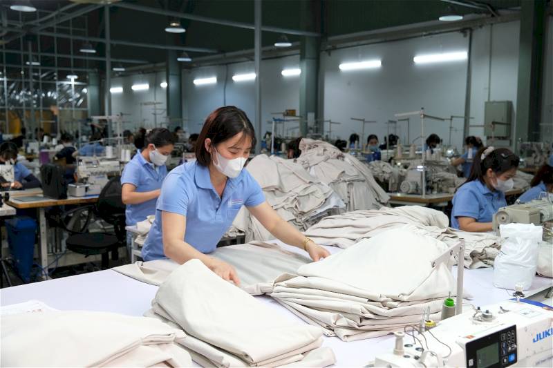 An Asian Chinese female worker in a blue uniform carefully inspecting fabric on a production line in a textile factory.