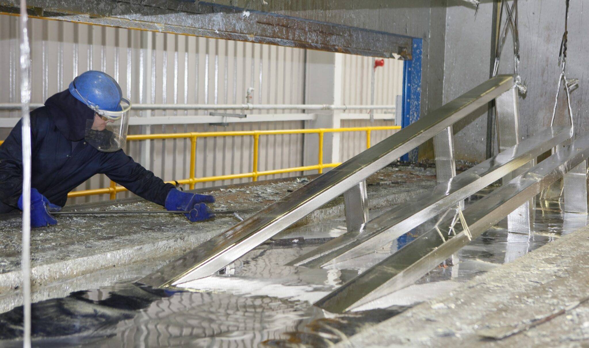 Worker applying a white zinc chloride chemical solution along steel parts in an industrial galvanizing line