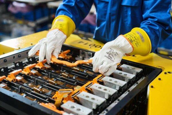 Technician wearing protective gloves working on battery assembly equipment in a manufacturing facility